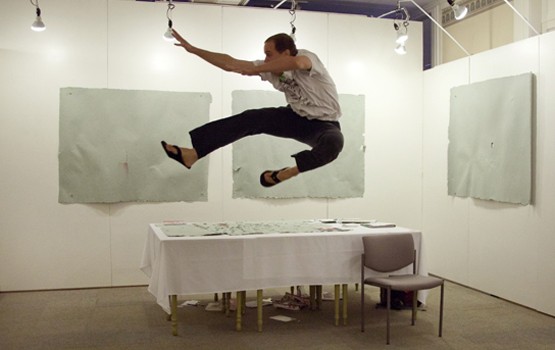 Thomas Gokey executes a jump kick in a gallery, in front of three panels from his art piece, “Total Amount of Money Rendered in Exchange for a Masters of Fine Arts Degree to the School of the Art Institute of Chicago, Pulped into Four Sheets of Paper.” Photo courtesy of Thomas Gokey.